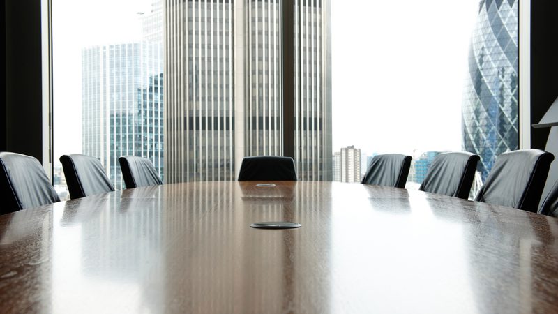 Boardroom table and chairs with city buildings beyond the windows, representing Company Formation and Governance at KMT Solicitors