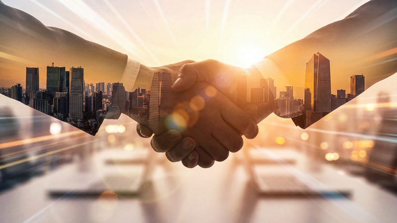 Handshake over a city skyline at sunrise, representing Mergers and Acquisitions at KMT Solicitors