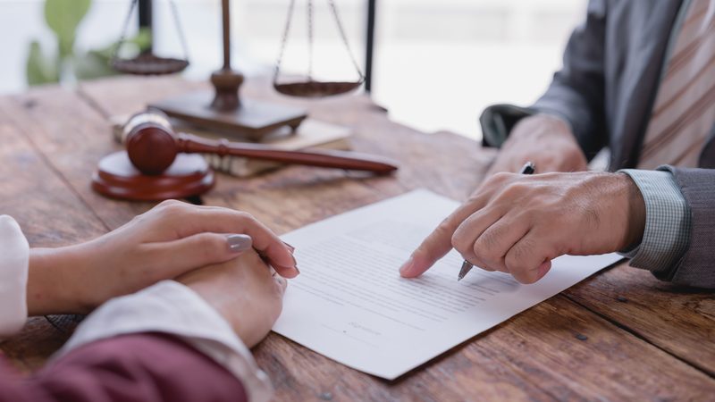 Lawyer pointing to a document for a client, with a gavel and scales on the desk, representing Extensions and Settlement at KMT Solicitors