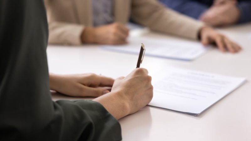 Person signing a document at a meeting table, representing Statutory Demands at KMT Solicitors