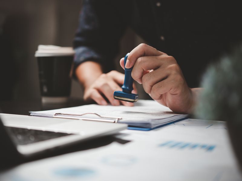 Hand stamping documents on a desk, representing regulatory and compliance advice at KMT Solicitors